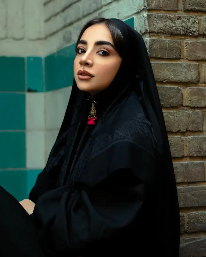 Portrait of an elegant Iranian woman wearing a black traditional hijab beside a tiled wall.