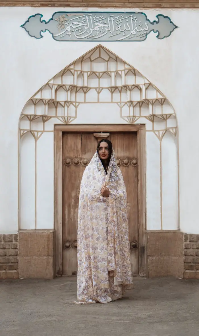 Elegant portrait of a woman in traditional Iranian attire standing at a decorative wooden doorway.