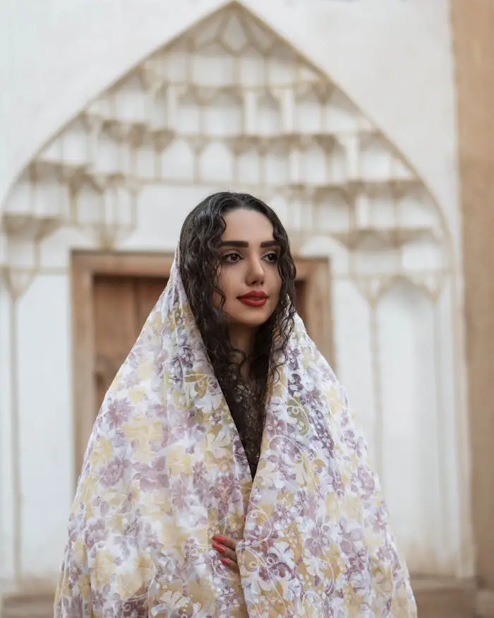 A woman in a floral shawl stands in front of Persian architecture in Isfahan, Iran.